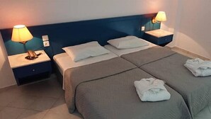 A hotel room with a double bed, two bedside tables with lamps, and a neatly made bed with towels. - Blue Sky Apartments (Hersonissos)