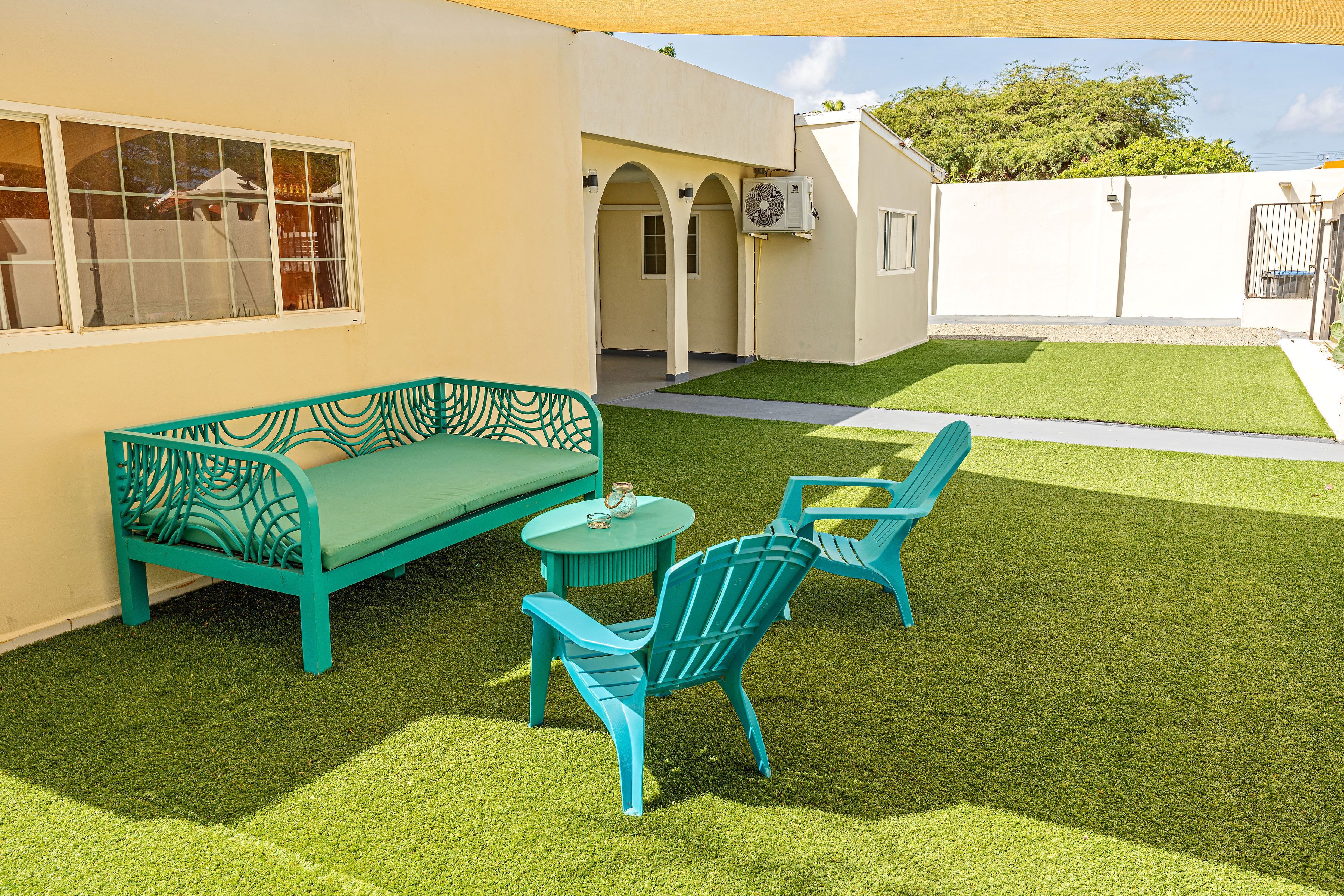 Un patio con césped verde, un sofá turquesa y sillas a juego.