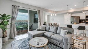 Un salon moderne avec un canapé d’angle gris, une table basse en marbre et un balcon offrant une vue dégagée.