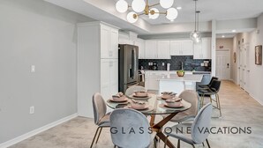 Une cuisine moderne avec des meubles blancs, un réfrigérateur noir et une table à manger en verre, accompagnée de six chaises.