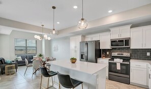 Una cocina moderna con armarios blancos, electrodomésticos de acero inoxidable y una isla central con taburetes de bar.