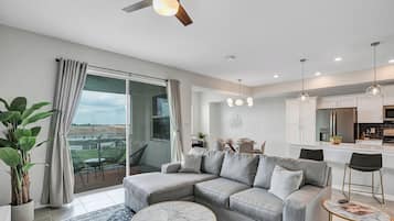 A modern living room with a grey sectional sofa, a marble coffee table, and a balcony with a view.