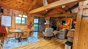 Interior de una cabaña de madera con comedor, chimenea y pared de piedra.