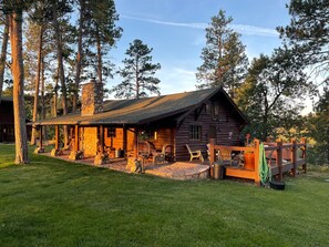 A rustic log cabin with a stone chimney, wooden deck, and outdoor seating area. - Big Horn Sheep Cottage Near Mt. Rushmore (Rapid City)