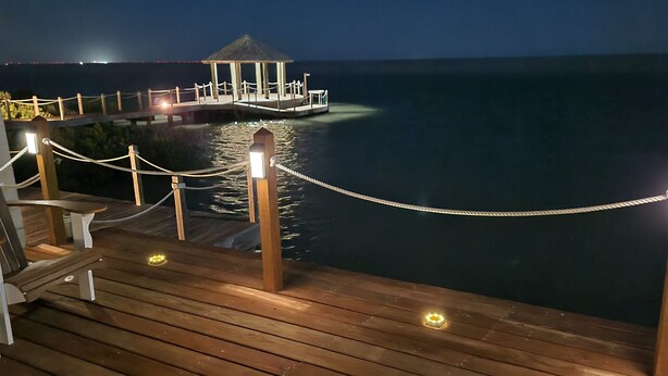 A wooden deck with a rope barrier, a gazebo, and a view of the ocean. - Waterfront Bay House Rental (Port Isabel)
