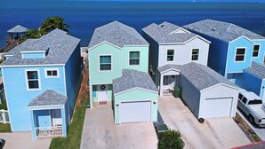 A row of light blue and white houses with grey roofs, a clear blue sky, and the ocean in the background. - Waterfront Bay House Rental (Port Isabel)