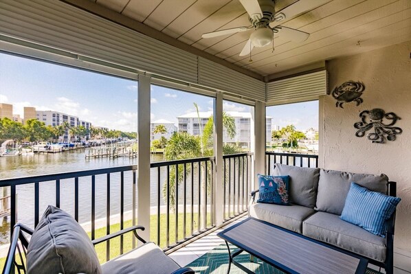 A balcony with a view of a marina, a sofa with cushions, and a ceiling fan.