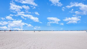 Una amplia playa de arena con cielo azul despejado y algunas nubes dispersas.