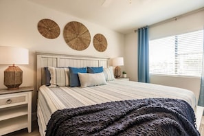 Un dormitorio con una cama, dos mesitas de noche, un ventanal con persianas y decoración en la pared.