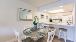 Cocina moderna con armarios blancos, una isla central y un comedor con una mesa redonda y sillas blancas.