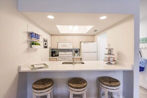 A modern kitchen with white cabinetry, a central island with stools, a microwave, and a refrigerator.