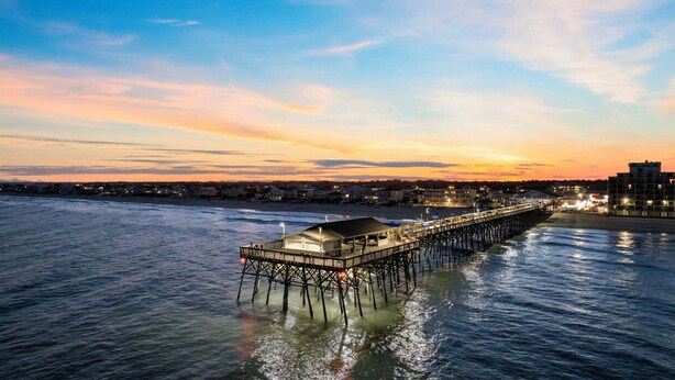 A pier extending into calm waters with a covered seating area and a building at the end. - Spacious Home with Private Pool, Steps from the Beach & Marsh Views (Murrells Inlet)