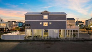 A two-story building with a flat roof, a balcony on the upper floor, and a covered outdoor area with a fence. - Spacious Home with Private Pool, Steps from the Beach & Marsh Views (Murrells Inlet)