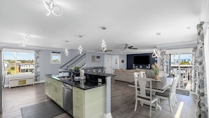 A modern kitchen with a central island, a dining area with a table and chairs, and a living room with a sofa. - Spacious Home with Private Pool, Steps from the Beach & Marsh Views (Murrells Inlet)