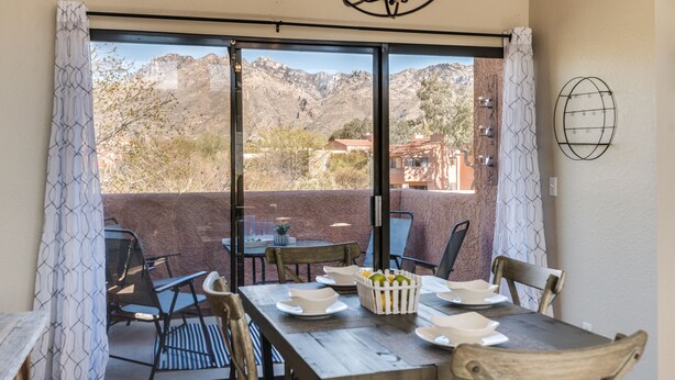 A dining area with a table set for four, a chandelier, and a view of mountains through large sliding glass doors. - Wake Up to Majestic Mountain Views in a Vaulted 2BR 2 BATH cozy getaway! (Tucson)