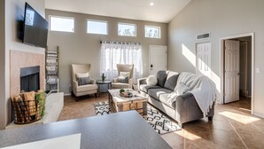 A spacious living room with a fireplace, a large sofa, a coffee table, and a TV mounted on the wall. - Wake Up to Majestic Mountain Views in a Vaulted 2BR 2 BATH cozy getaway! (Tucson)