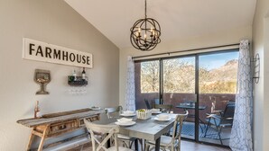 A dining area with a rustic wooden table and chairs, a chandelier, and a 'FARMHOUSE' sign on the wall. - Wake Up to Majestic Mountain Views in a Vaulted 2BR 2 BATH cozy getaway! (Tucson)
