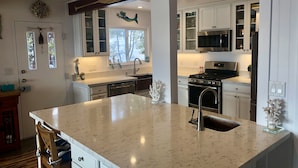 A modern kitchen with white cabinetry, a large island with a sink, stainless steel appliances, and decorative wall art. - Lake front chalet-incredible view, sleeps 12! (Homewood)