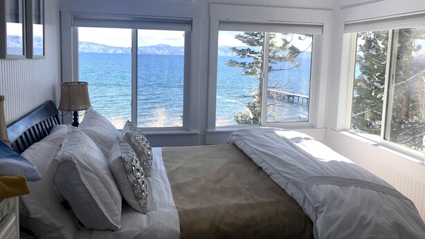 A bedroom with a bed, a lamp, and large windows overlooking a body of water. - Lake front chalet-incredible view, sleeps 12! (Homewood)