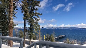 A deck with a view of a lake, snow-covered ground, and a bridge in the distance. - Lake front chalet-incredible view, sleeps 12! (Homewood)