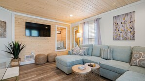 Een moderne woonkamer met een hoekbank, een flatscreen televisie, een grote spiegel en een houten plafond.