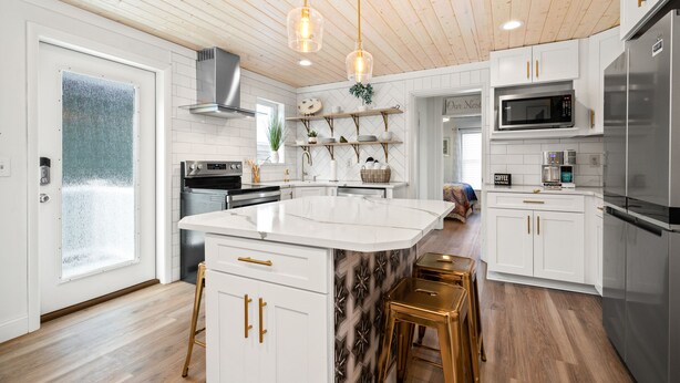 Een moderne keuken met witte kasten, een centraal eiland, roestvrijstalen apparatuur en een houten plafond.