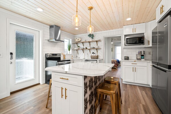A modern kitchen with white cabinetry, a central island, stainless steel appliances, and a wooden ceiling.