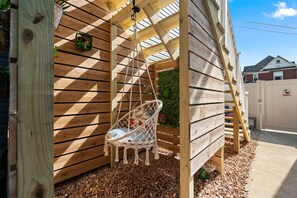 Une structure en bois avec une chaise suspendue, une petite plante et une échelle en bois.