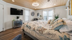 Een slaapkamer met een houten plafond, een bed met bloemenbeddelsels, een televisie aan de muur en een nachtkastje met een plant.