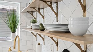 Een keuken met een houten plank met borden en een kom, een gouden kraan en een potplant.