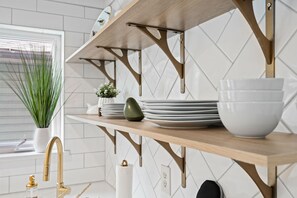 A kitchen with a wooden shelf holding plates and a bowl, a gold faucet, and a potted plant.