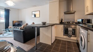 A modern kitchen with a built-in oven, microwave, and dishwasher. There is a dining area with a black sofa and a glass table. - No 10 (Mansfield)