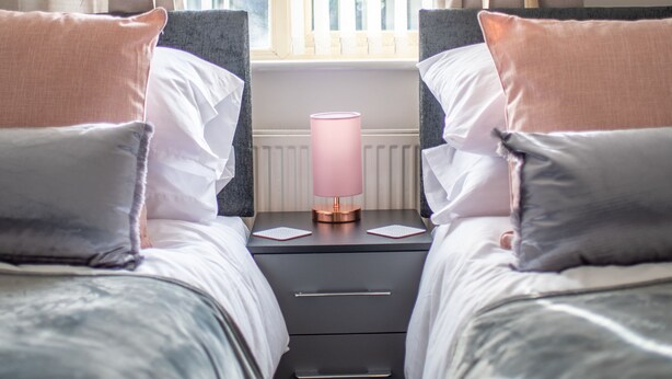 A bedroom with two beds, a bedside table with a lamp, and a window with blinds. - No 10 (Mansfield)