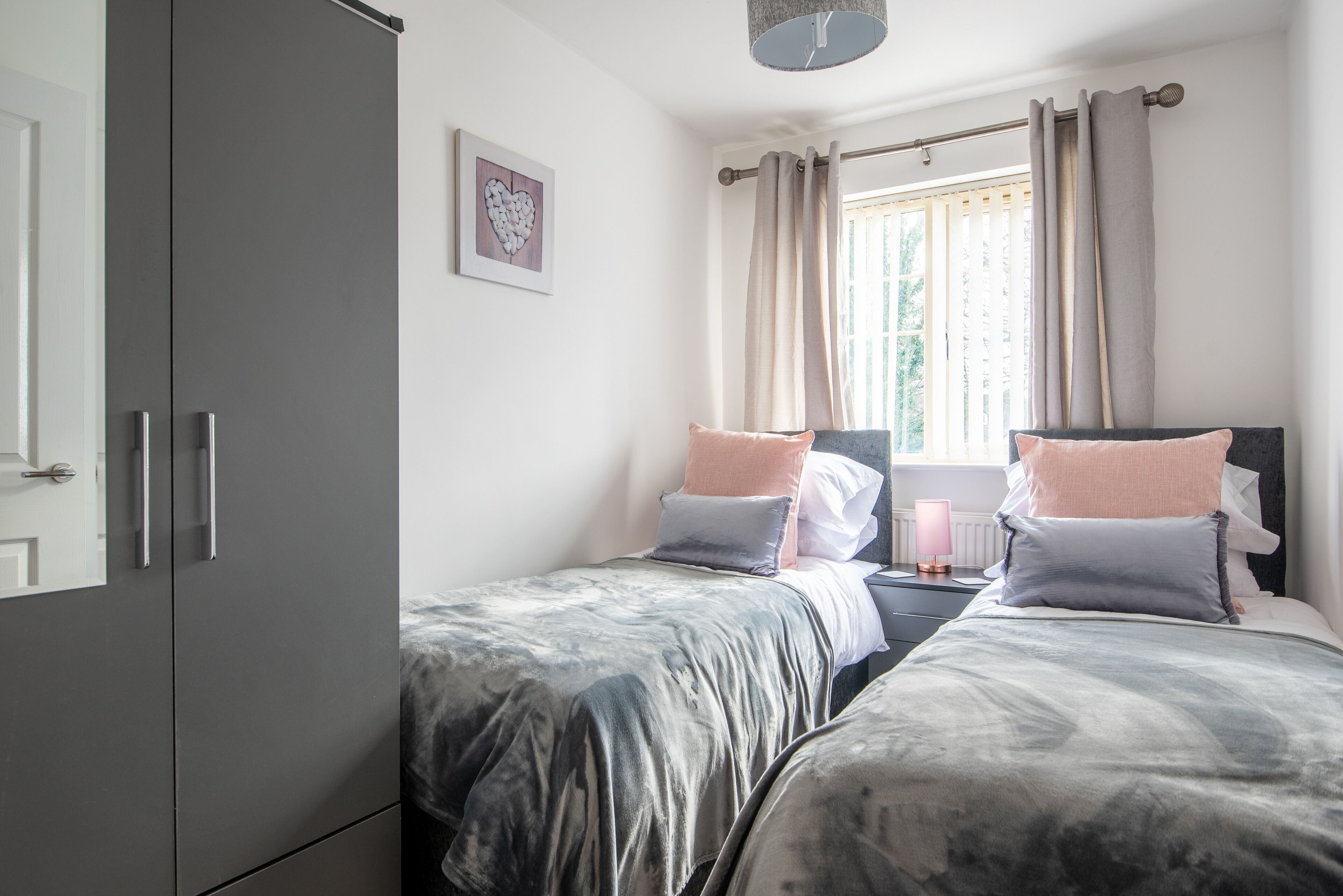 Een slaapkamer met twee bedden, een kledingkast, een nachtkastje met een lamp en een raam met gordijnen.