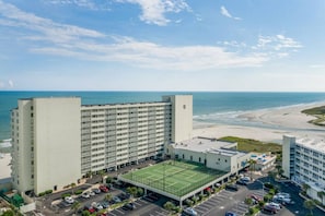 Hotel alto com quadra de tênis e estacionamento, com vista para uma praia.