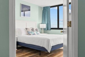 Quarto com cama, mesa de cabeceira, luminária e janela com cortinas.