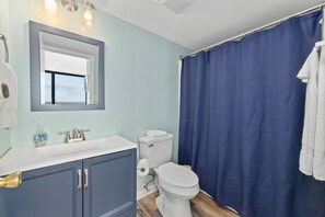 Een badkamer met een witte wastafel, blauwe kastjes, een wit toilet en een blauw douchegordijn.
