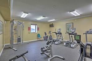 Een fitnessruimte met diverse trainingsapparaten, een stoel en een televisie aan de muur.