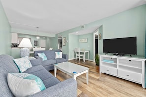 Een moderne woonkamer met een grijze bank, een witte salontafel en een televisie op een witte dressoir.