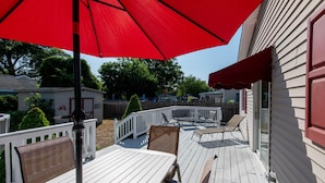 A wooden deck with outdoor furniture, a red umbrella, and a white railing.