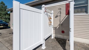 A white metal gate in front of a house with beige siding and a window with red shutters.
