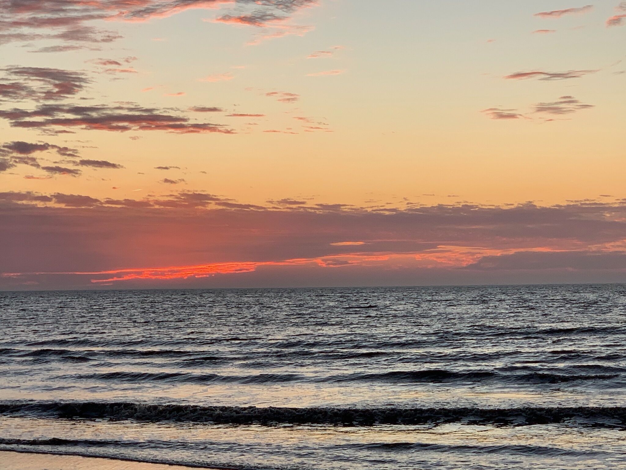 A sunset over a calm sea with waves gently lapping at the shore.
