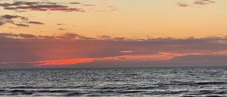 A sunset over a calm sea with waves gently lapping at the shore.