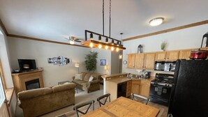 A compact kitchen with wooden cabinets, a dining table, and a sofa in the living area. - Will it be ICE AXE, CRAWLER, NORDIC? 1200MGPS-Mtn Views! On River! BBQ & yard! (Ouray)