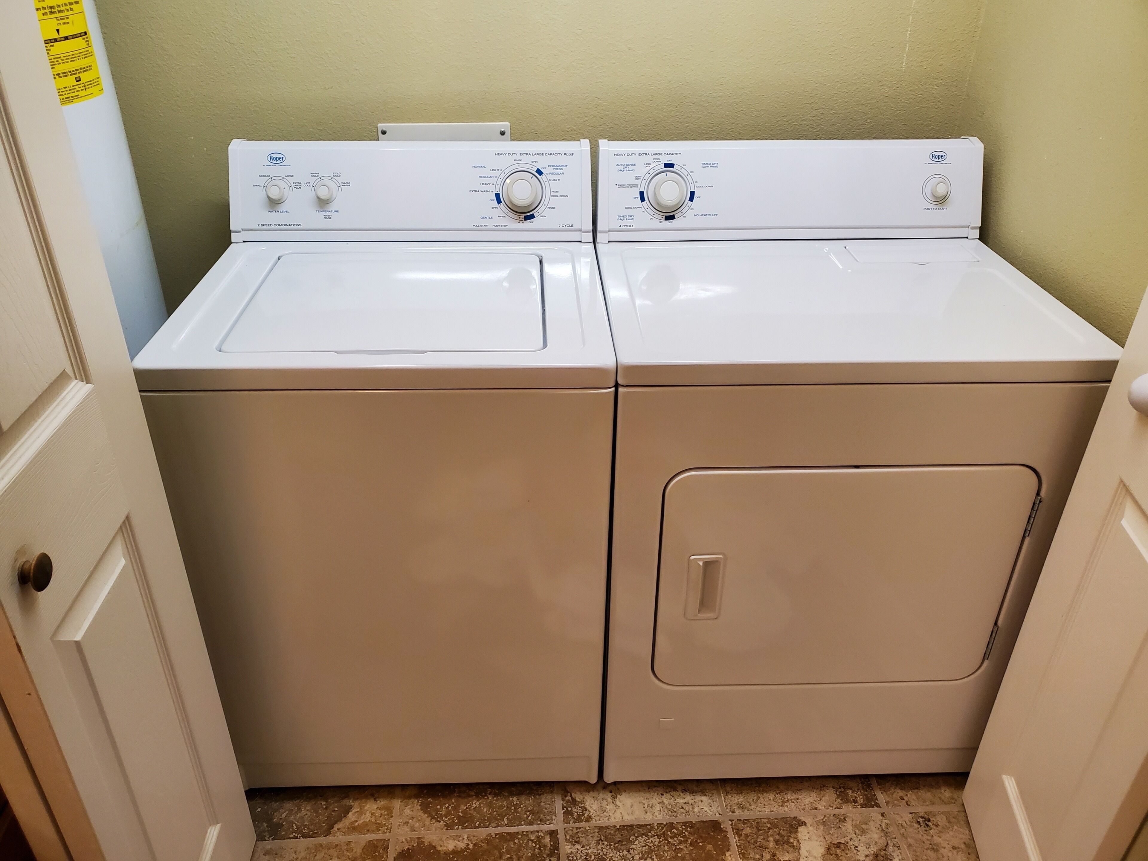 A laundry room with two front-loading washers and dryers, a tiled floor, and a door on the left.