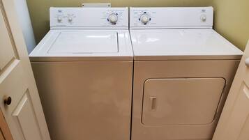 A laundry room with two front-loading washers and dryers, a tiled floor, and a door on the left.