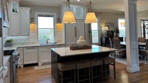 A spacious kitchen with white cabinetry, a central island with bar stools, pendant lighting, and a view to a dining area. - SOUTHERN LIVING! Newly renovated! Private with Mountain views-sleeps 16 (Kingston)