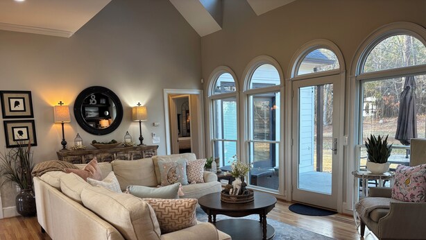 A spacious living room with a beige sofa, a coffee table, and a view through large arched windows. - SOUTHERN LIVING! Newly renovated! Private with Mountain views-sleeps 16 (Kingston)