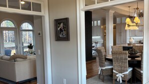 A spacious living area with a wooden floor, a sofa, a dining table with wicker chairs, and a kitchen in the background. - SOUTHERN LIVING! Newly renovated! Private with Mountain views-sleeps 16 (Kingston)