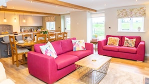 A spacious living area with two bright pink sofas, a wooden coffee table, and a dining area with a wooden table and chairs. - The Patches (Shrewsbury)